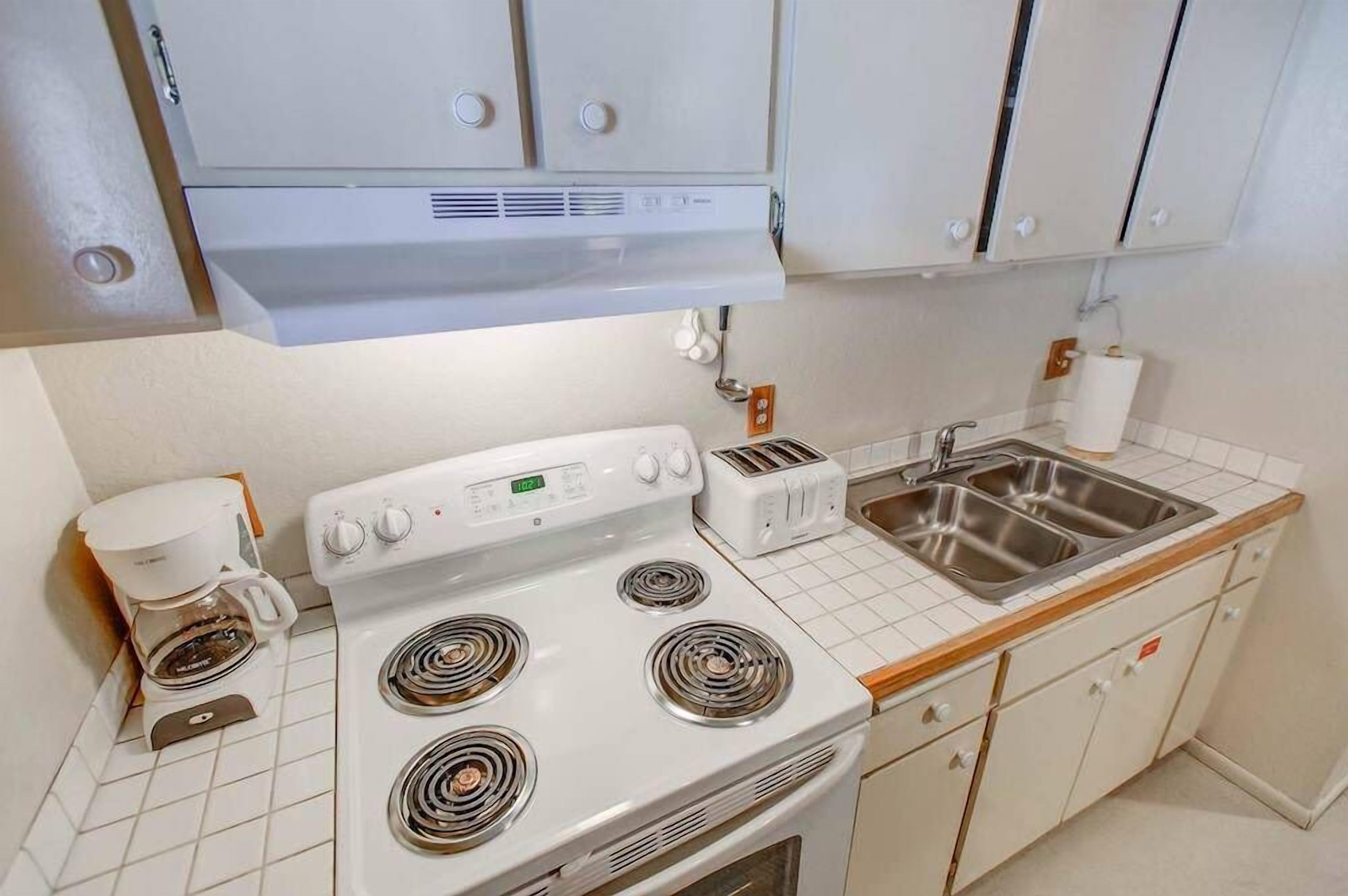 A kitchen with a stove, toaster, sink, and cabinets.