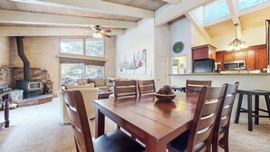 A spacious living room with a wooden dining table, comfortable seating, a fireplace, and a kitchen area with wooden cabinets and modern appliances.