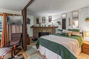 A bedroom with a bed, a chair, a fireplace, and a television.