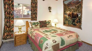 Un dormitorio con una cama grande, cortinas florales, un cuadro de un alce y una mesita de noche con una lámpara.