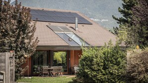 A modern house with a sloped roof, solar panels, and a large glass door leading to an outdoor dining area.