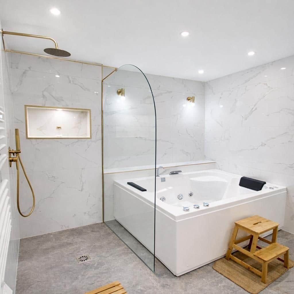 Een moderne badkamer met een douche in een glazen cabine, een vrijstaand bad en een houten kruk.