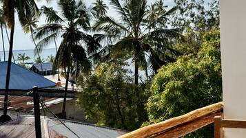 A wooden staircase leading to a terrace with a view of palm trees and a beach.