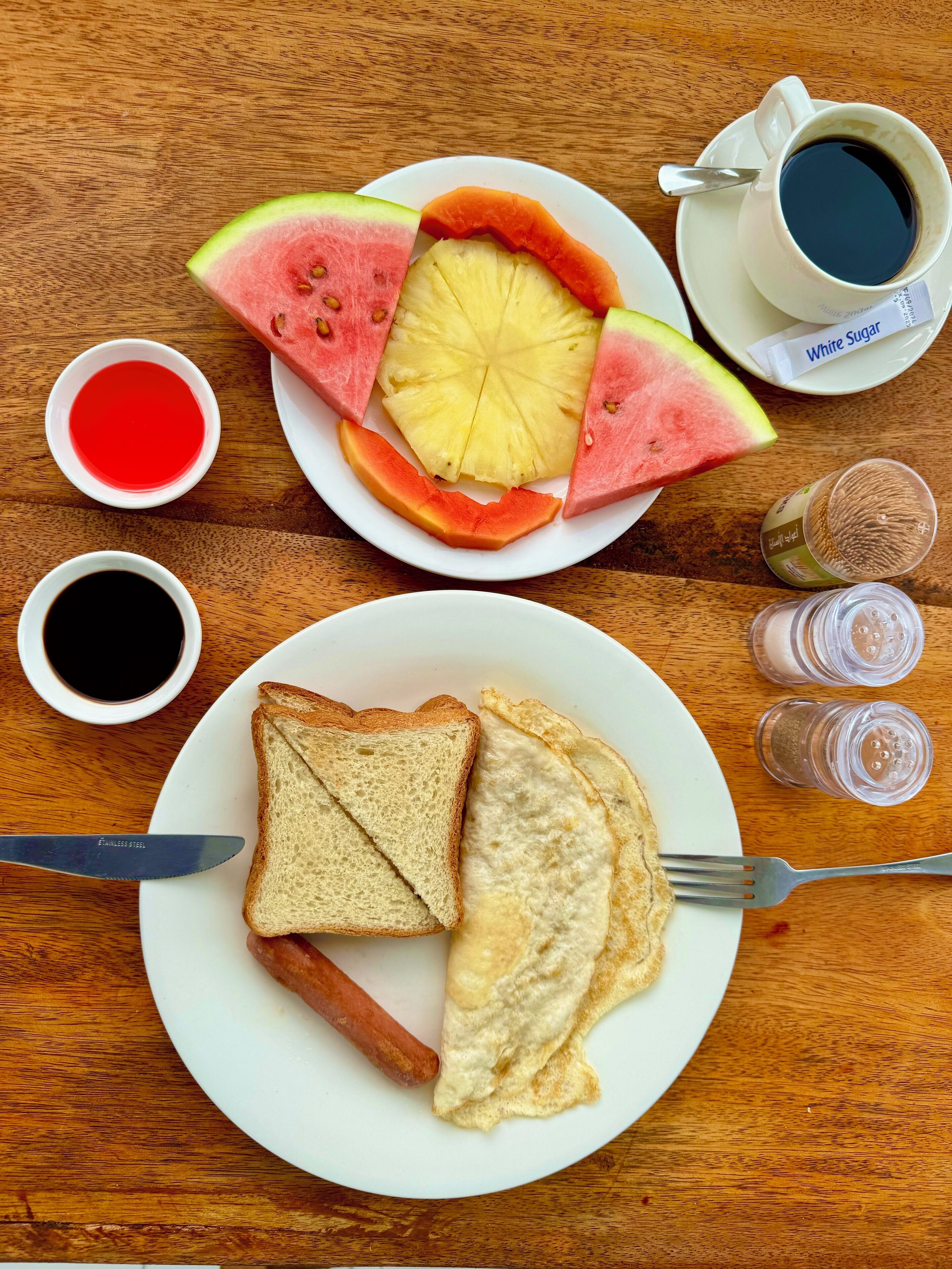 A breakfast setting with toast, eggs, sausage, and fruit on a wooden table.