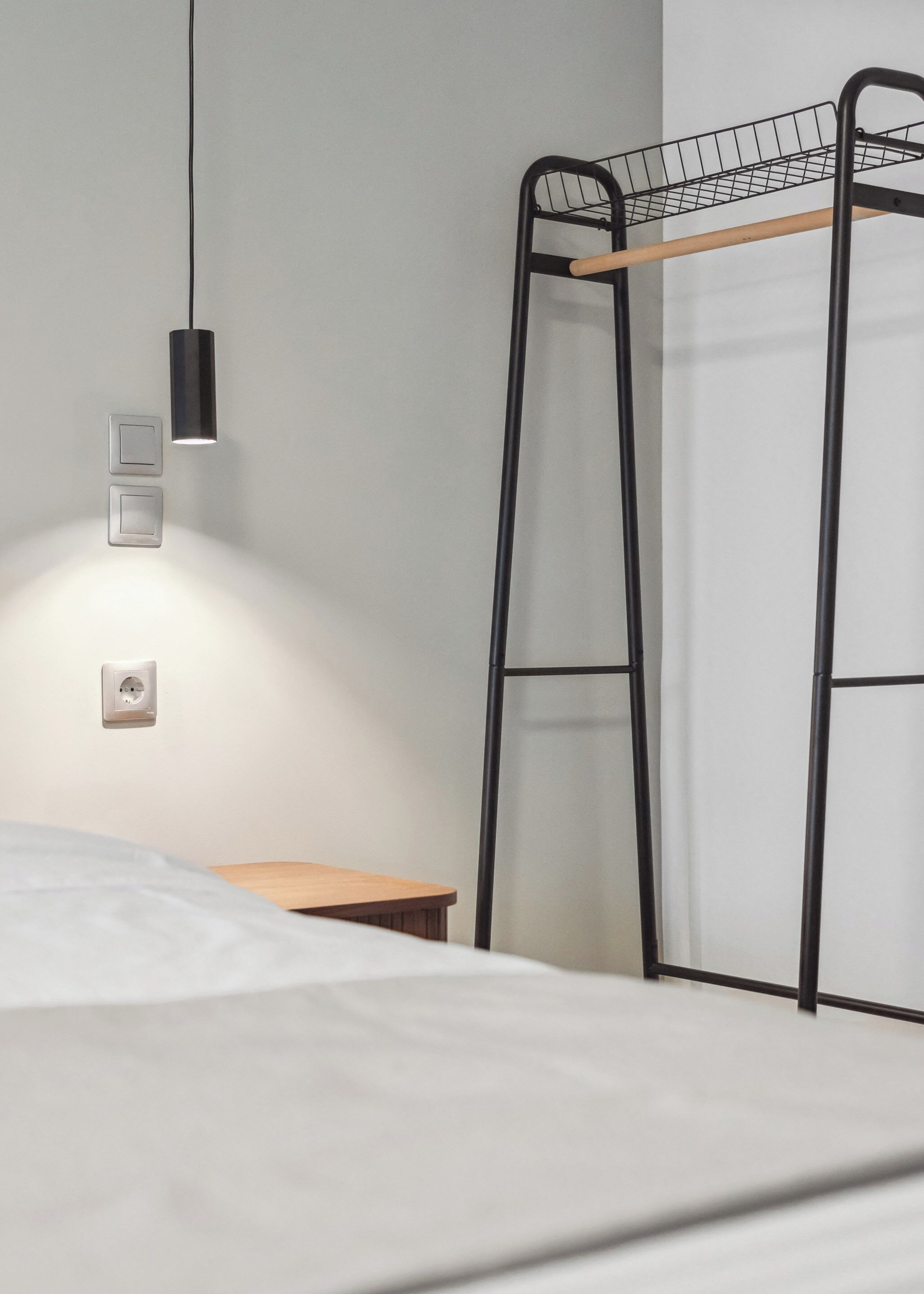 A bunk bed with a wooden ladder, a bedside table, and a wall-mounted light fixture.