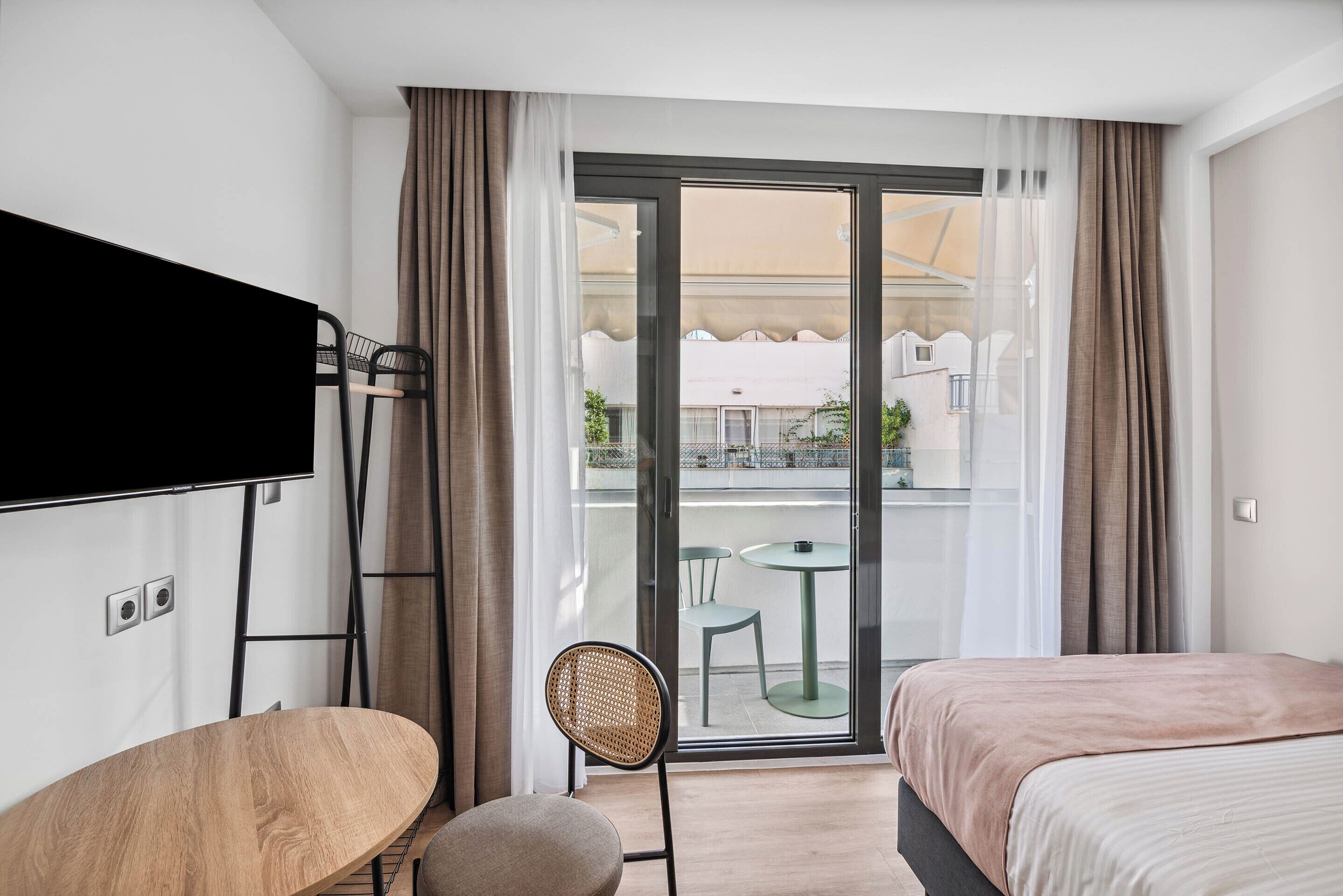 Une chambre d’hôtel comprenant un lit, un bureau, une chaise, une télévision et un balcon avec une table et des chaises.