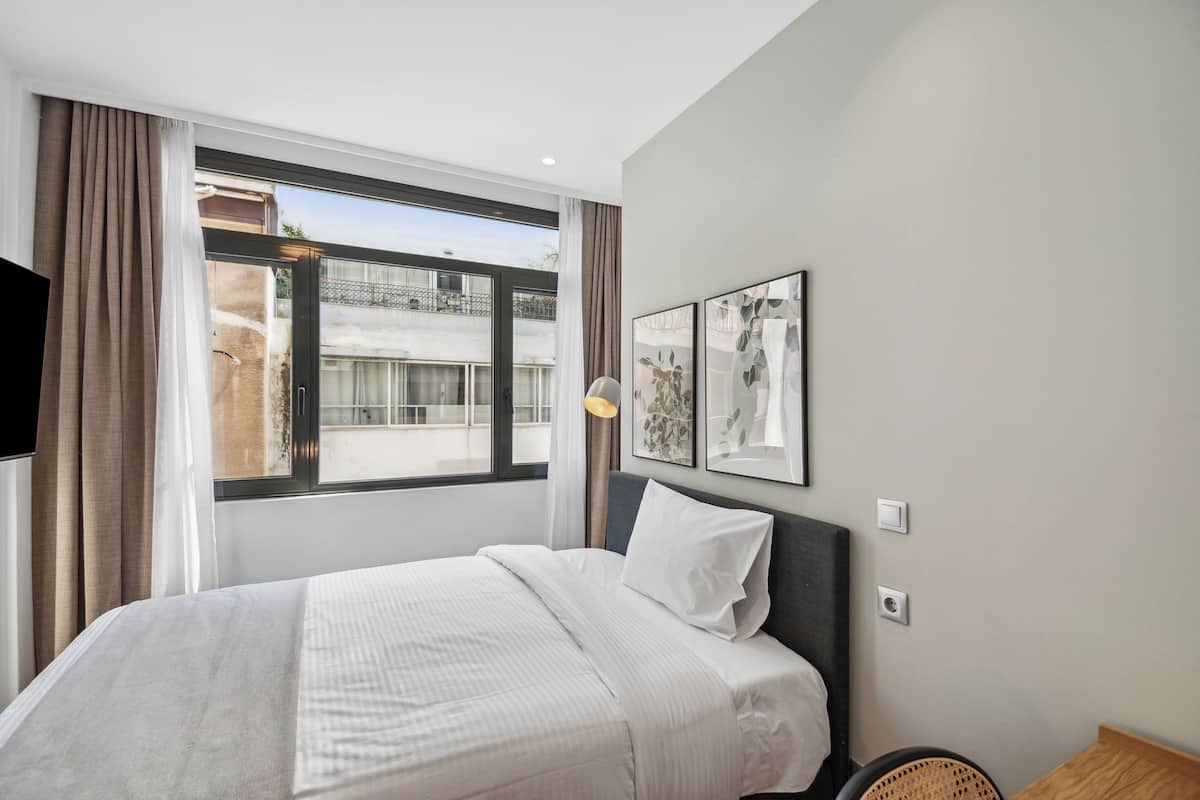 A hotel room with a large bed, a window with curtains, a wall-mounted TV, and framed artwork.