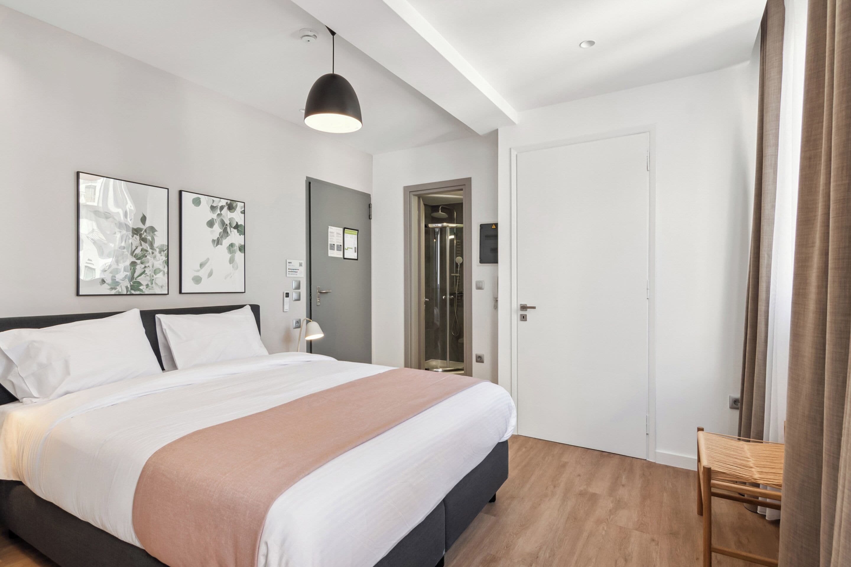 A modern bedroom with a large bed, a desk, and a shower area.