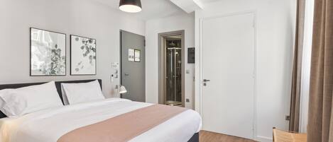 A modern bedroom with a large bed, a desk, and a shower area.