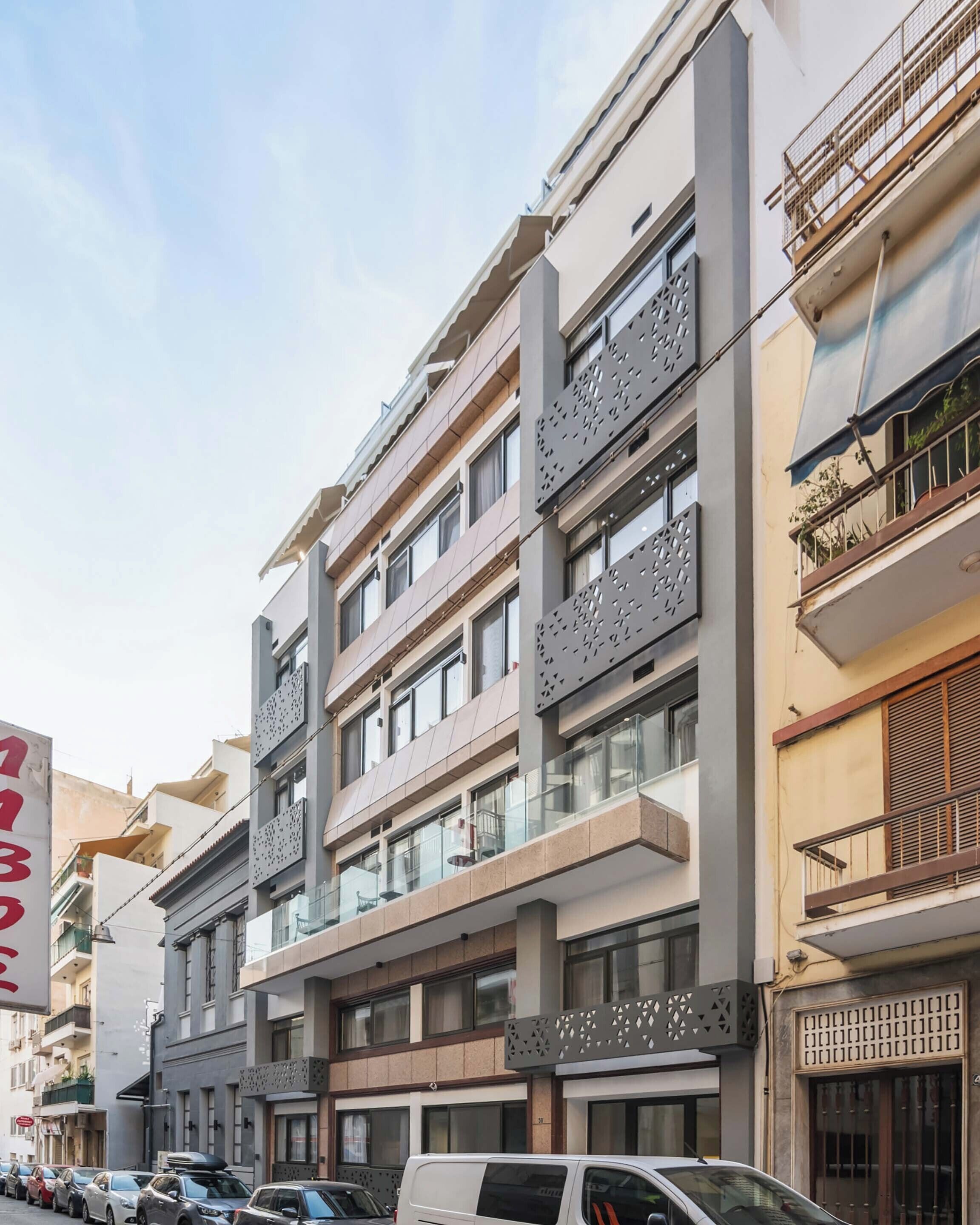 Un edificio de varios pisos con balcones, ventanas amplias y un estacionamiento con automóviles.