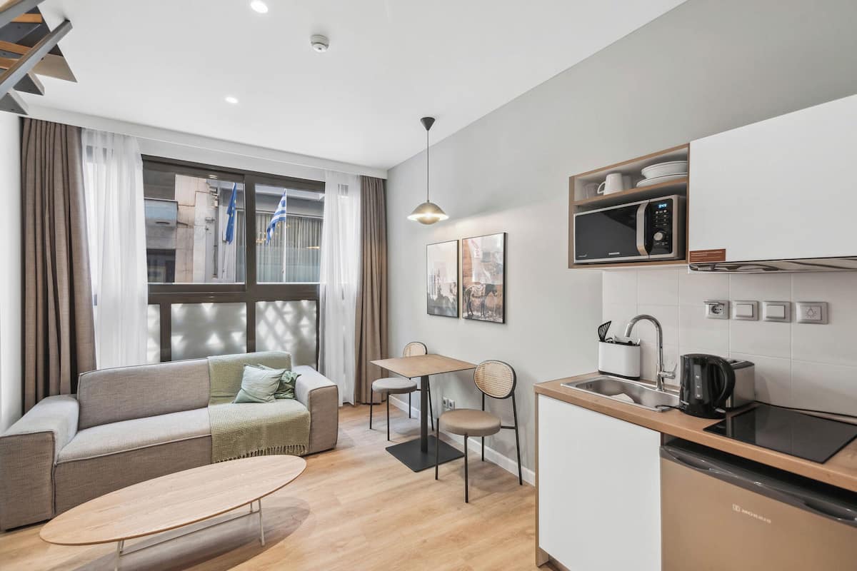 A compact living space with a sofa, a small dining table, a kitchen area with a microwave and sink, and a window with curtains.