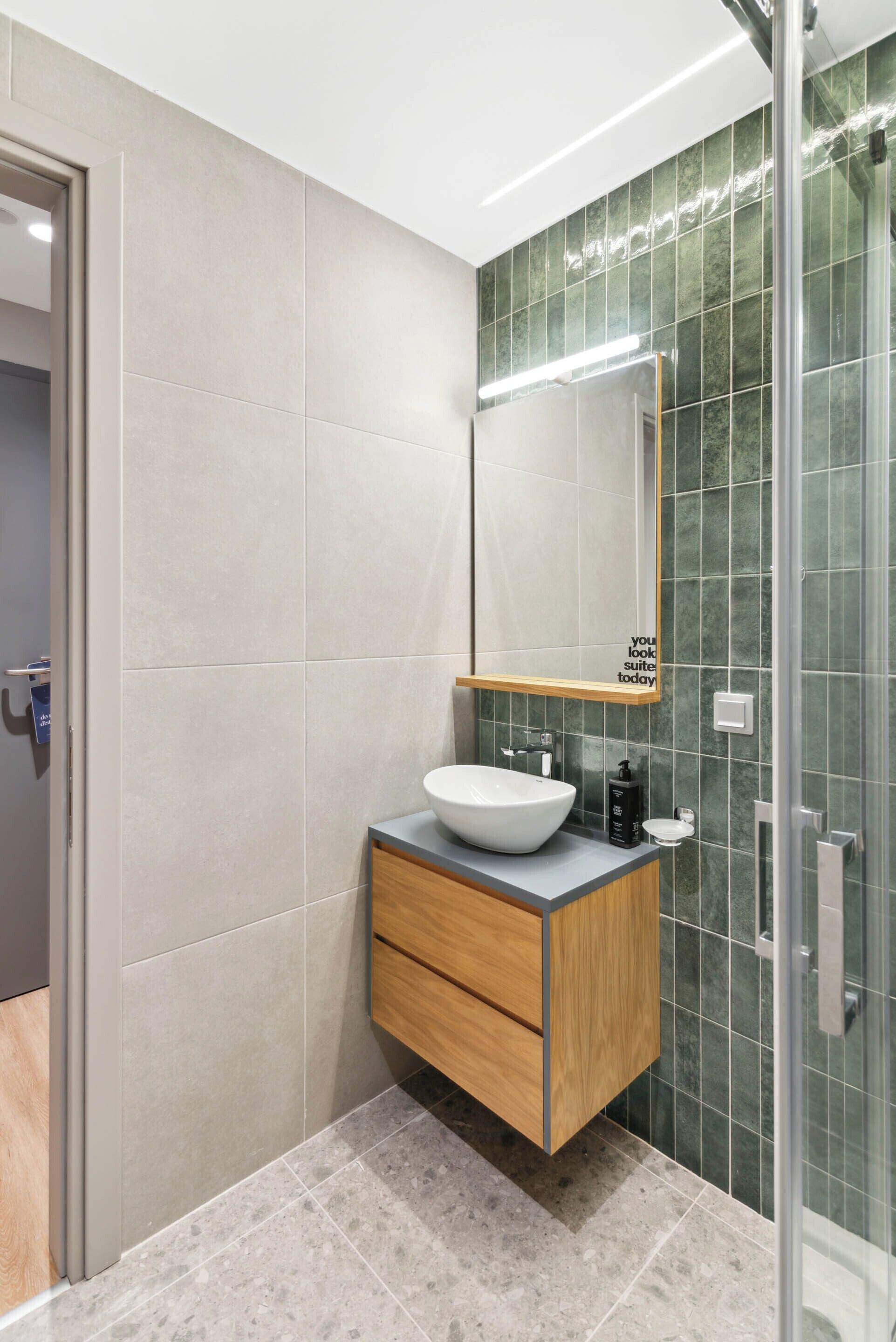 A modern bathroom with a white sink, wooden vanity, and a glass shower enclosure.