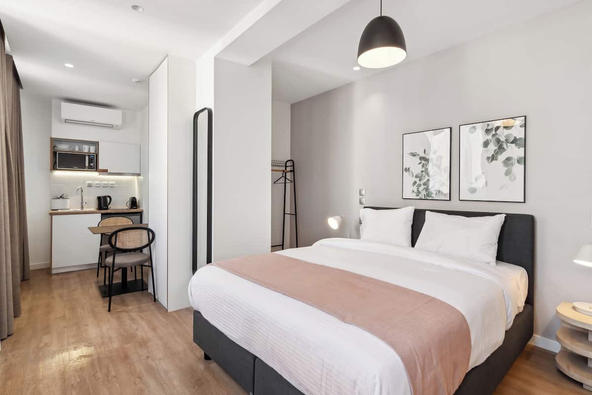 A modern hotel room with a large bed, bedside table, and a small kitchenette area.