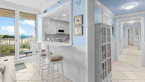 Une cuisine moderne avec des meubles blancs, un coin bar avec des tabourets et une vue sur un balcon extérieur, accessible par de grandes portes-fenêtres coulissantes.