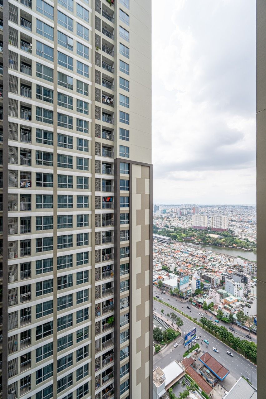 A high-rise building with multiple balconies and a view of a cityscape with various buildings and a river.