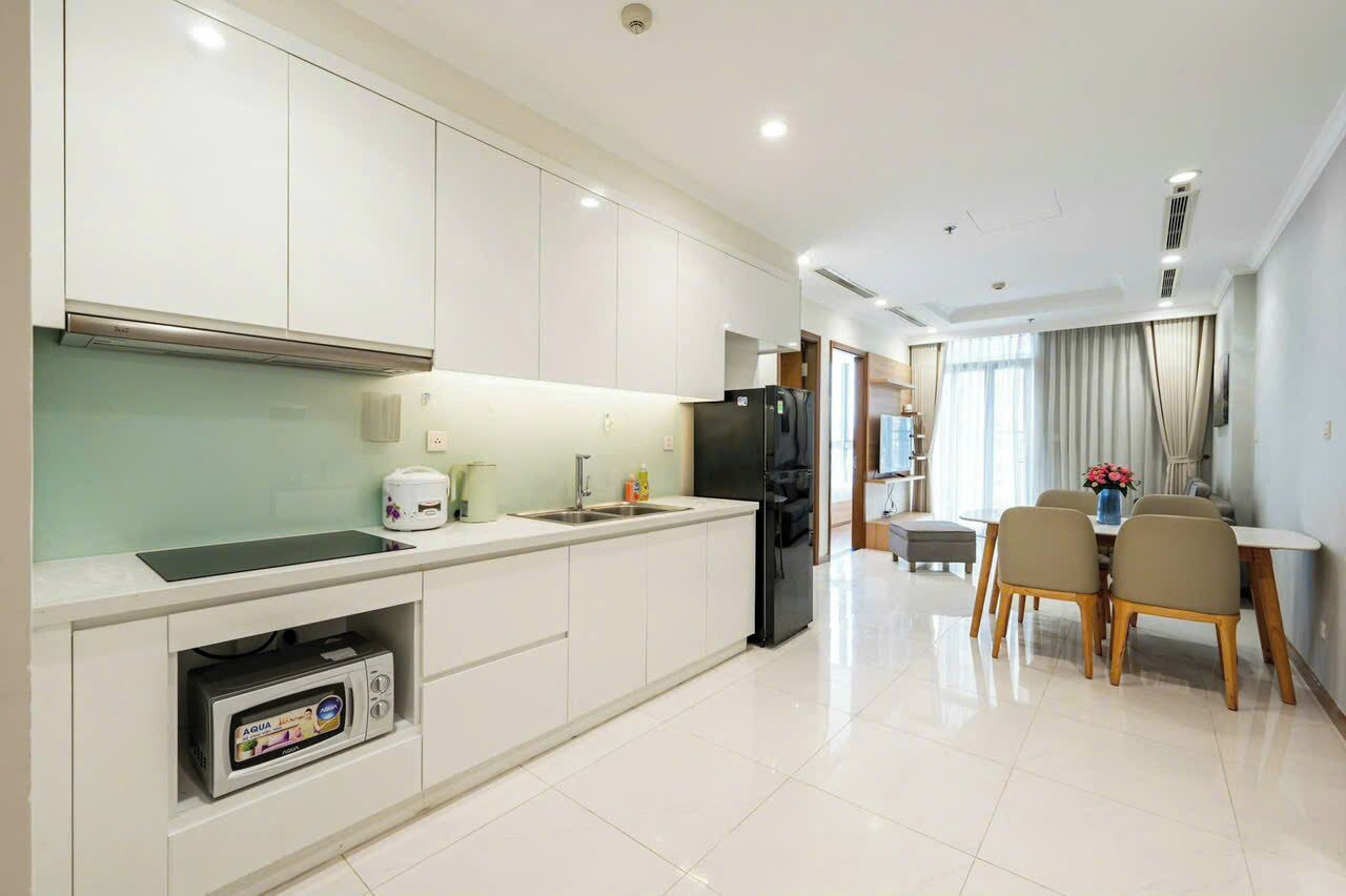 A modern kitchen with white cabinetry, a built-in microwave, and a dining area with a table and chairs.