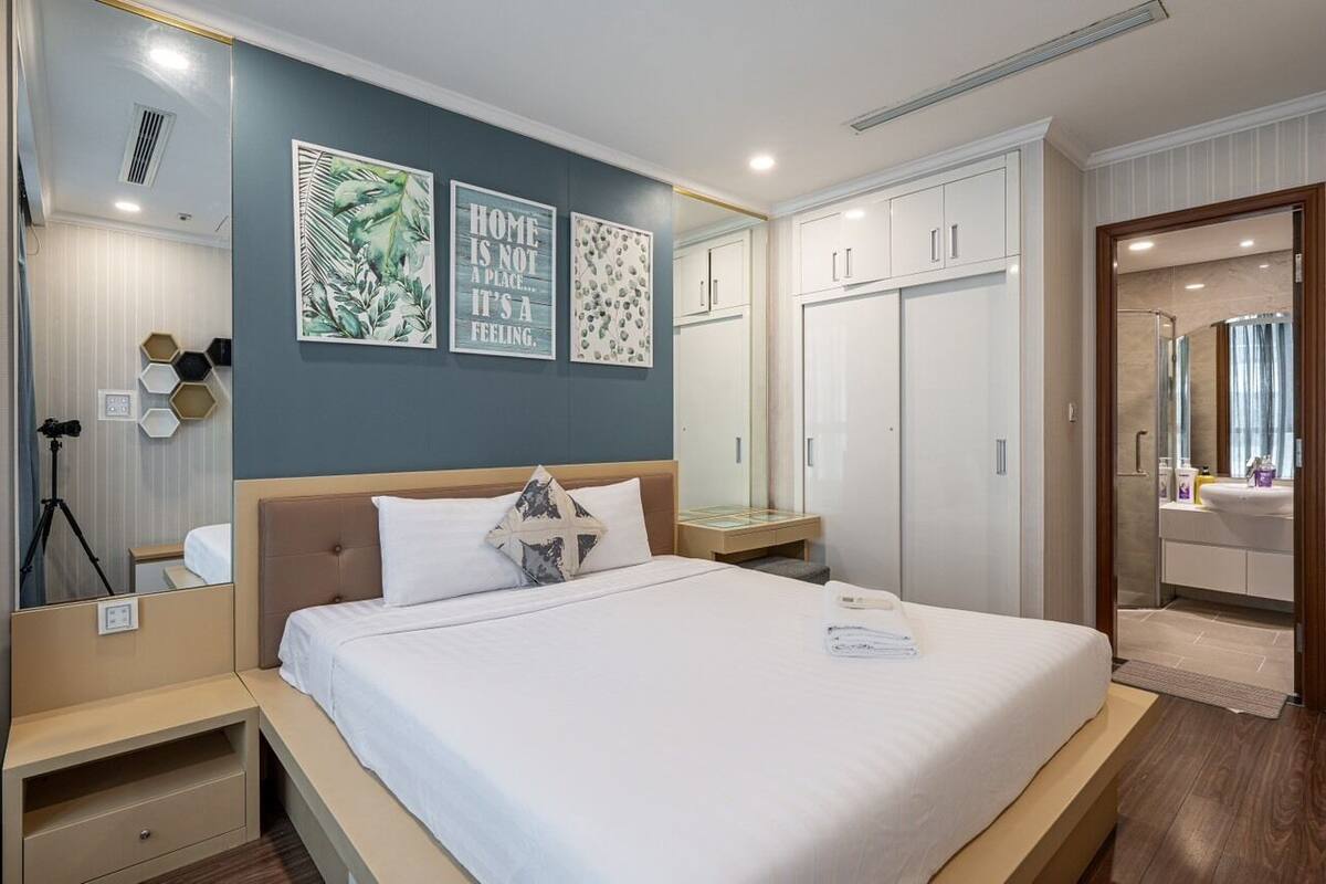 A hotel room with a bed, a wardrobe, a vanity with a mirror, and artwork on the wall.