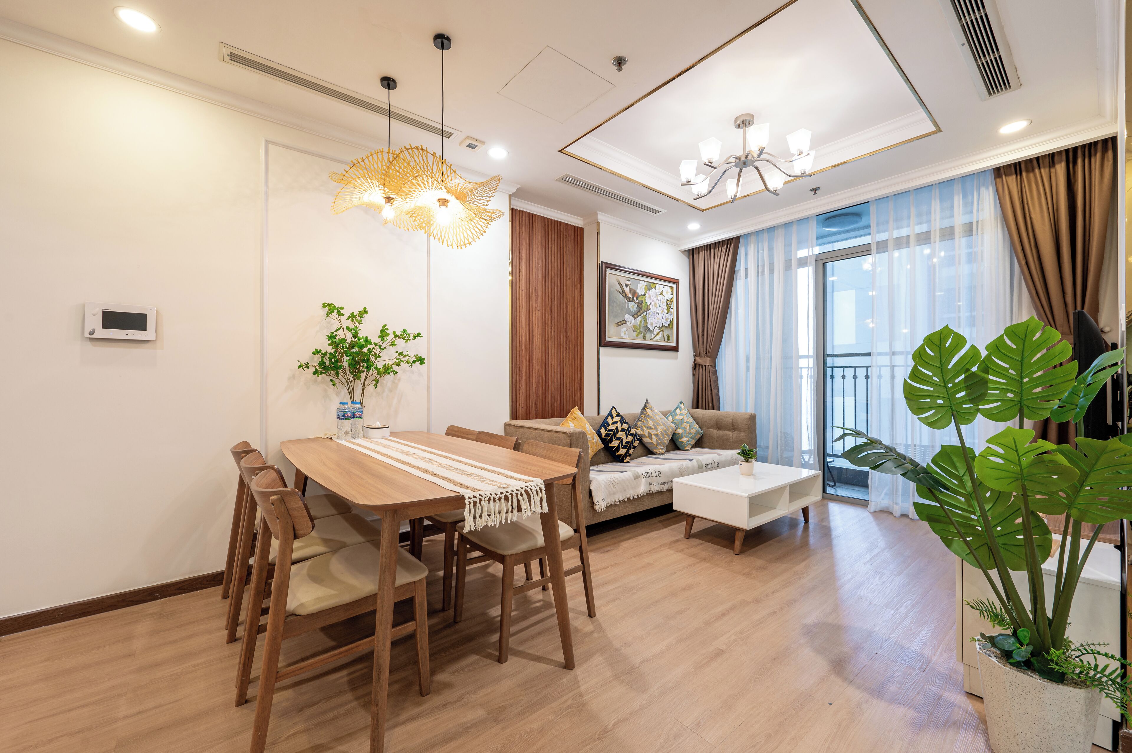 A modern living room with a wooden dining table, sofa, and large windows with curtains.