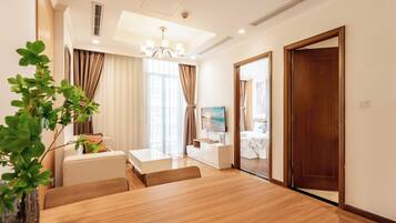 Una habitación de hotel moderna con una mesa de comedor de madera, un sofá, un televisor y un ventanal con cortinas.