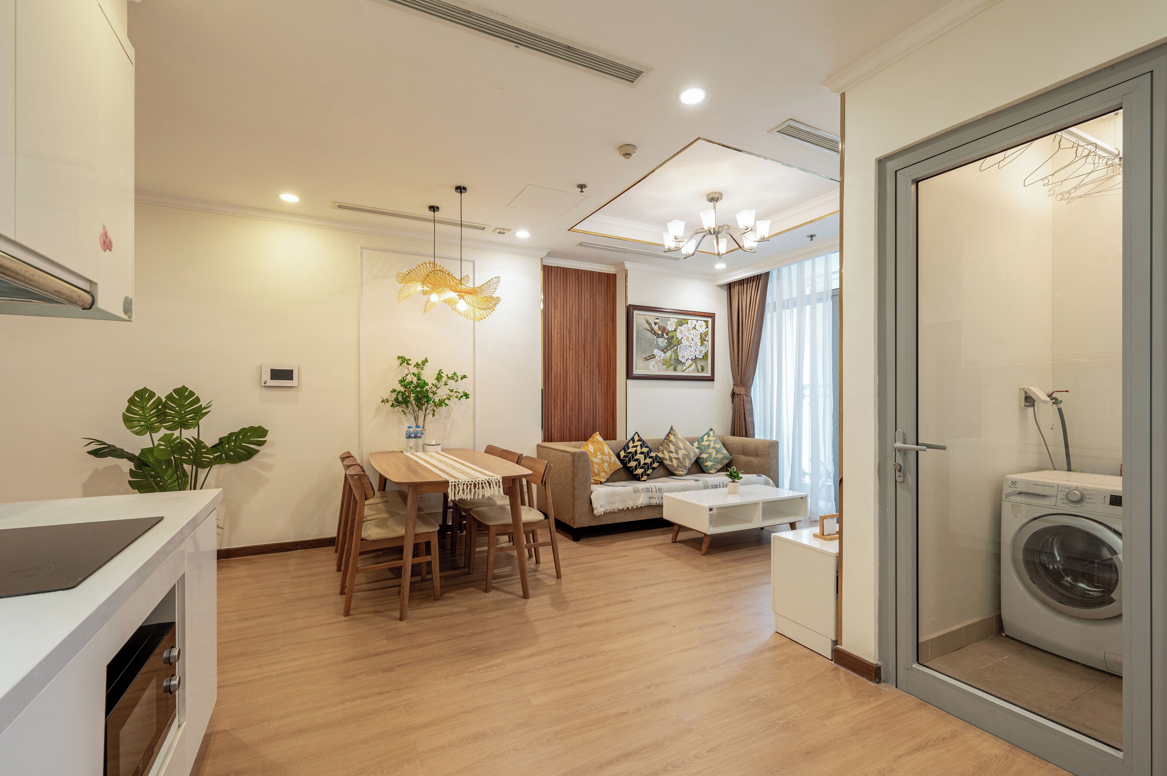A modern living room with a dining area, a sofa set, a coffee table, and a washing machine in a separate room.