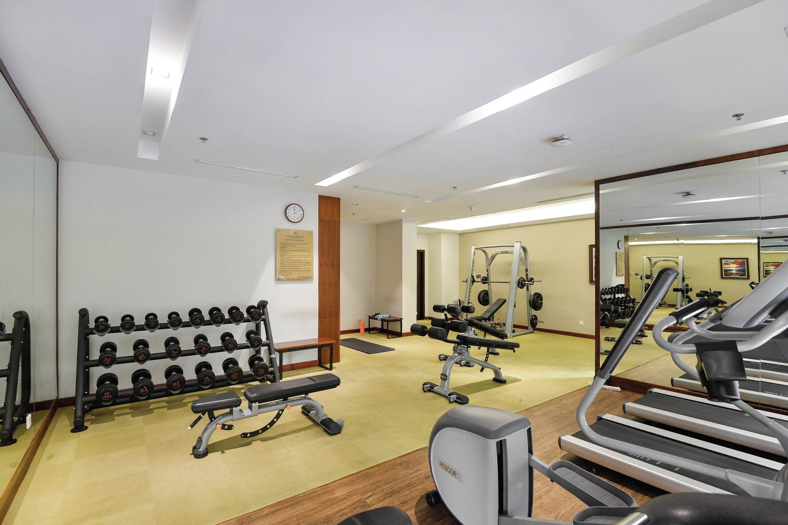 Un gimnasio con cintas de correr, máquinas de pesas y un estante con mancuernas.