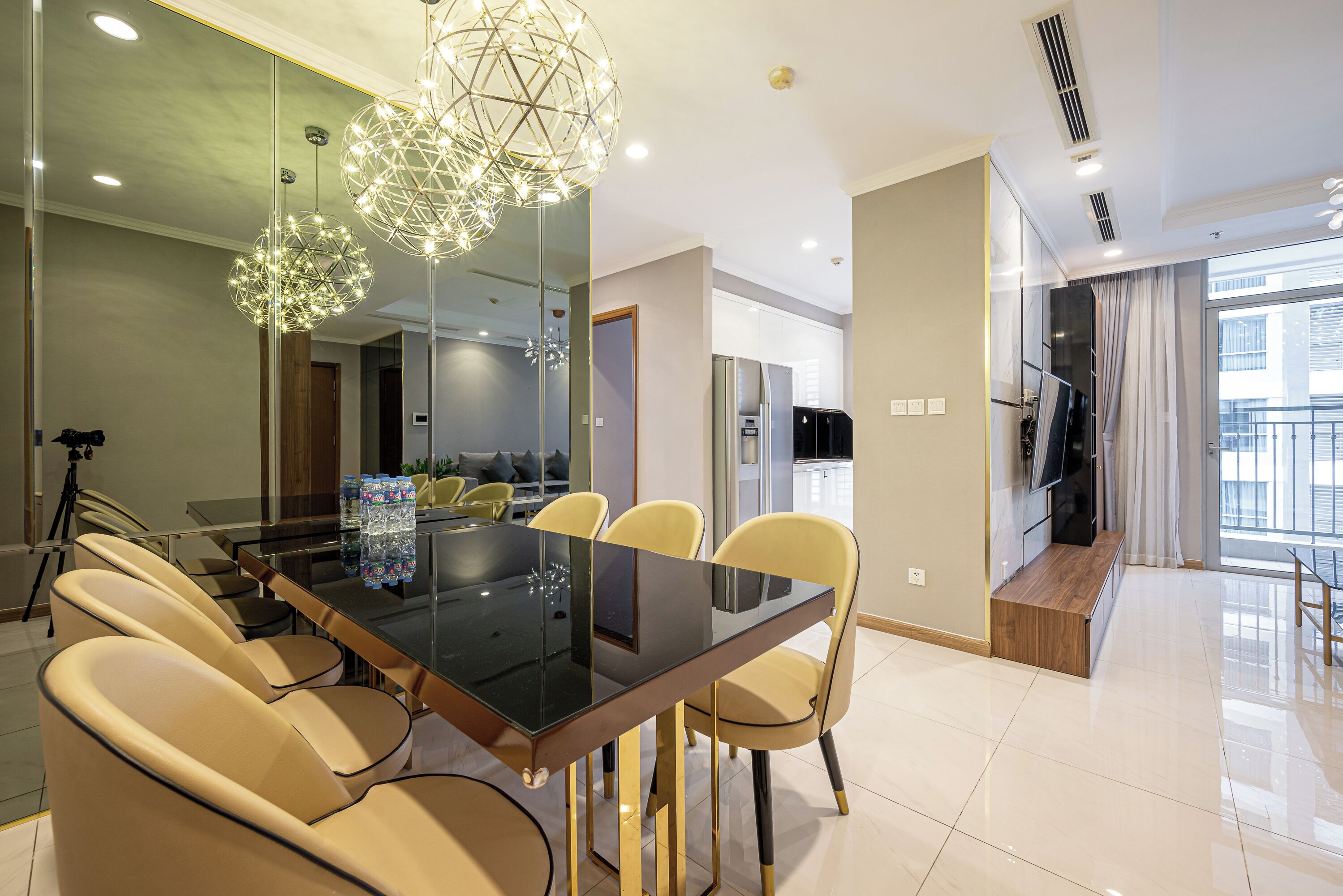 A modern dining area with a glass table, beige chairs, and a geometric chandelier.