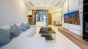 A modern living room with a sofa, a glass coffee table, and a cityscape painting on the wall. - Vinhomes Cozy Apartment (Ho Chi Minh City)
