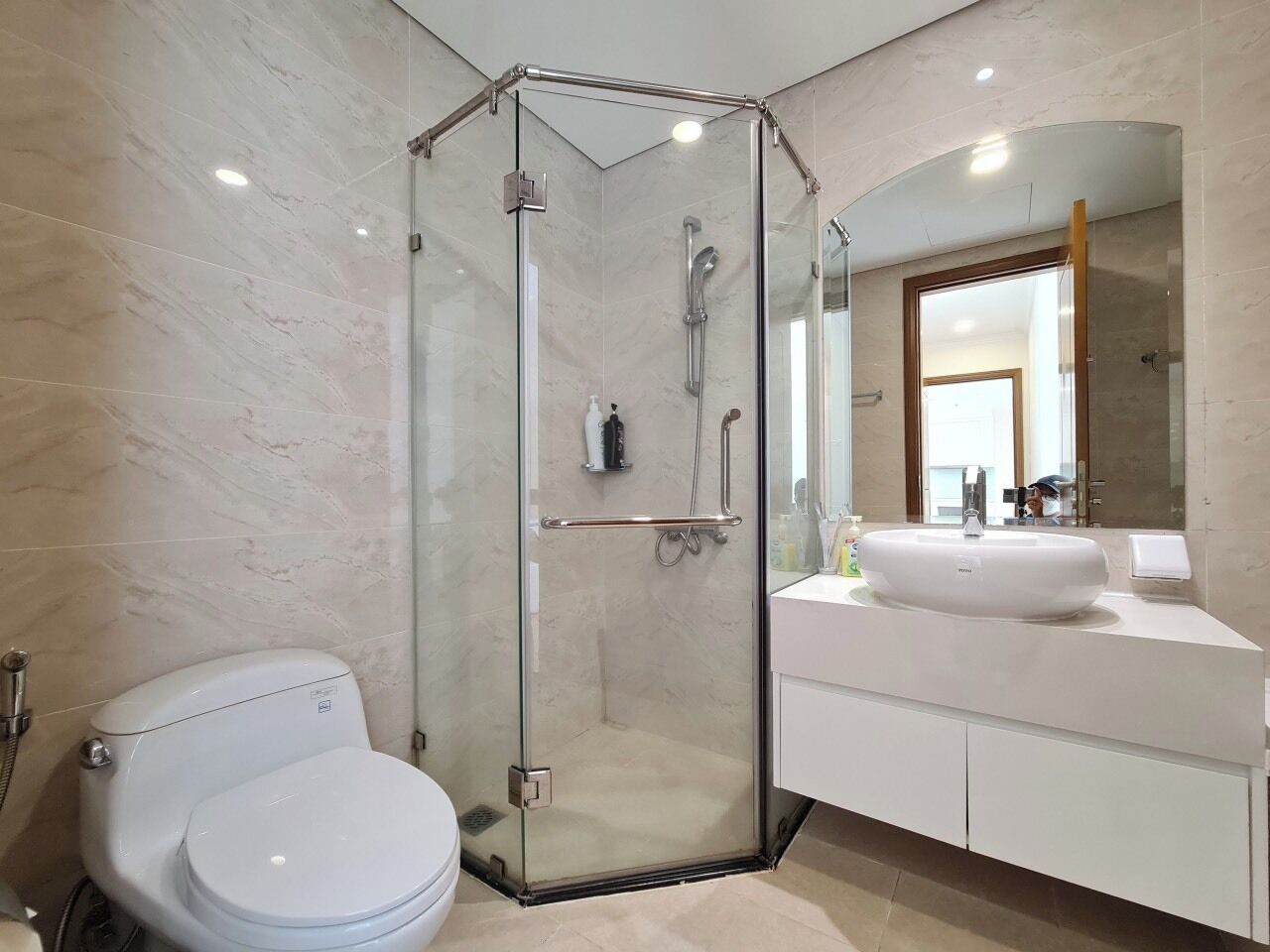 Un baño moderno con ducha de vidrio, inodoro blanco y tocador con un espejo grande y lavamanos.