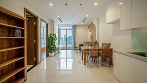 A modern kitchen with a dining area, wooden shelves, and a large window. - Vinhomes Cozy Apartment (Ho Chi Minh City)
