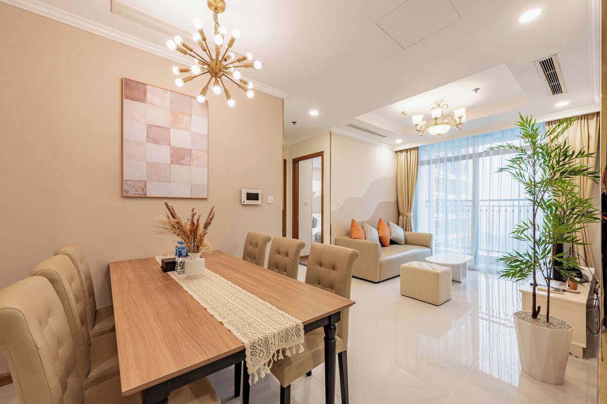 A modern living room with a wooden dining table, beige sofas, and a large window with curtains.