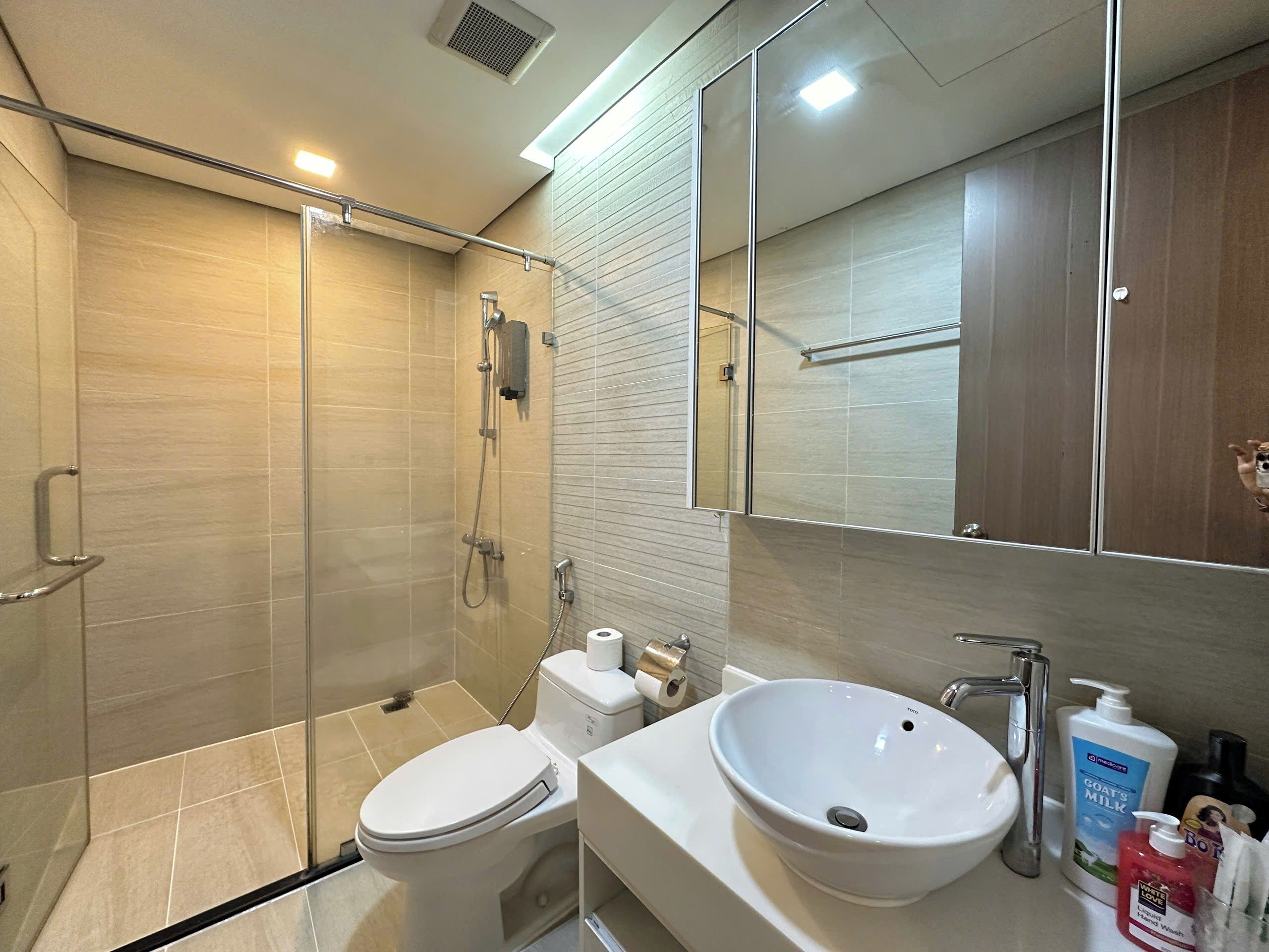 A modern bathroom with a glass-enclosed shower, a white toilet, and a sink with toiletries.