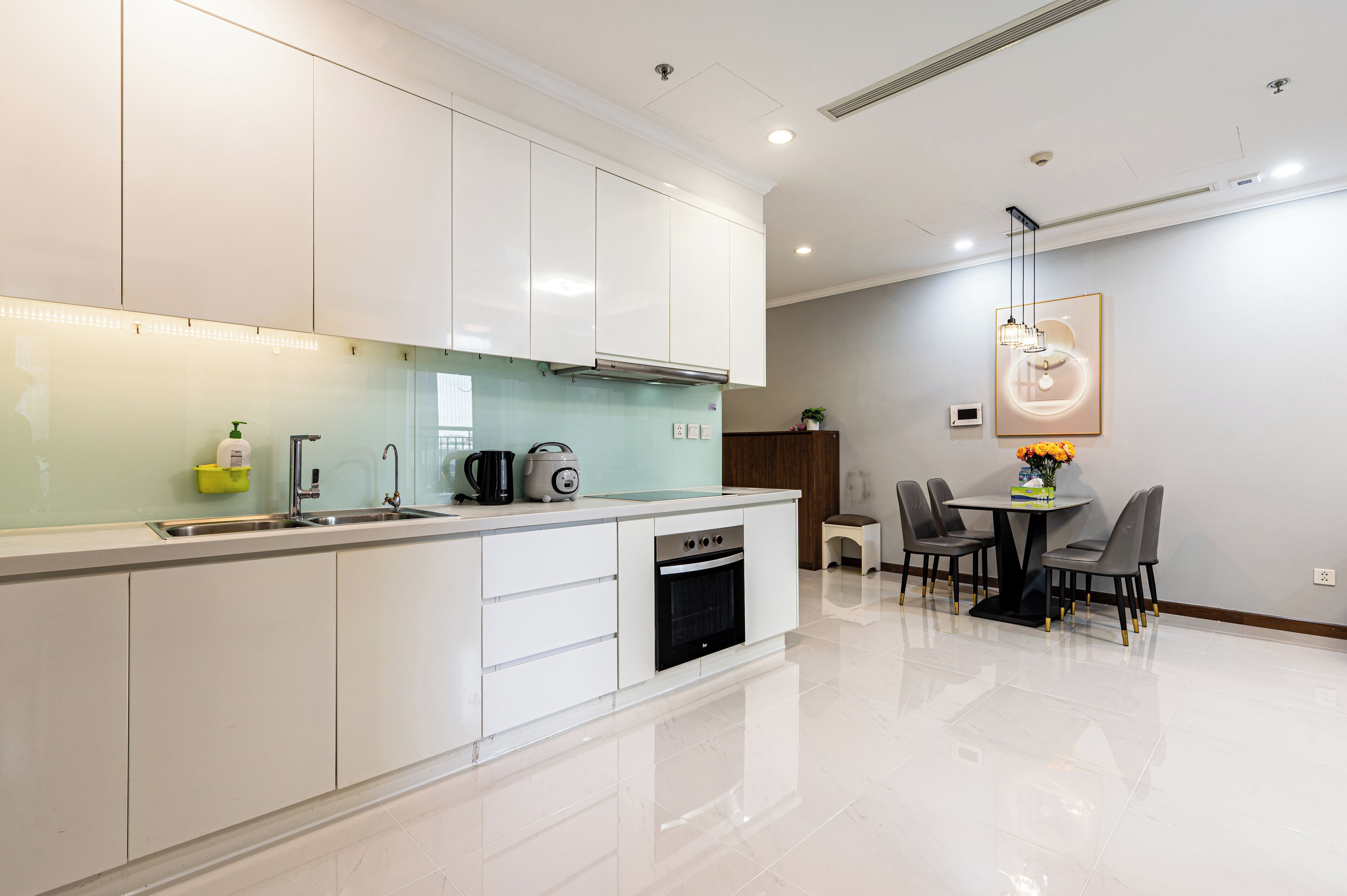 A modern kitchen with white cabinets, a built-in oven, and a dining area with a table and chairs.