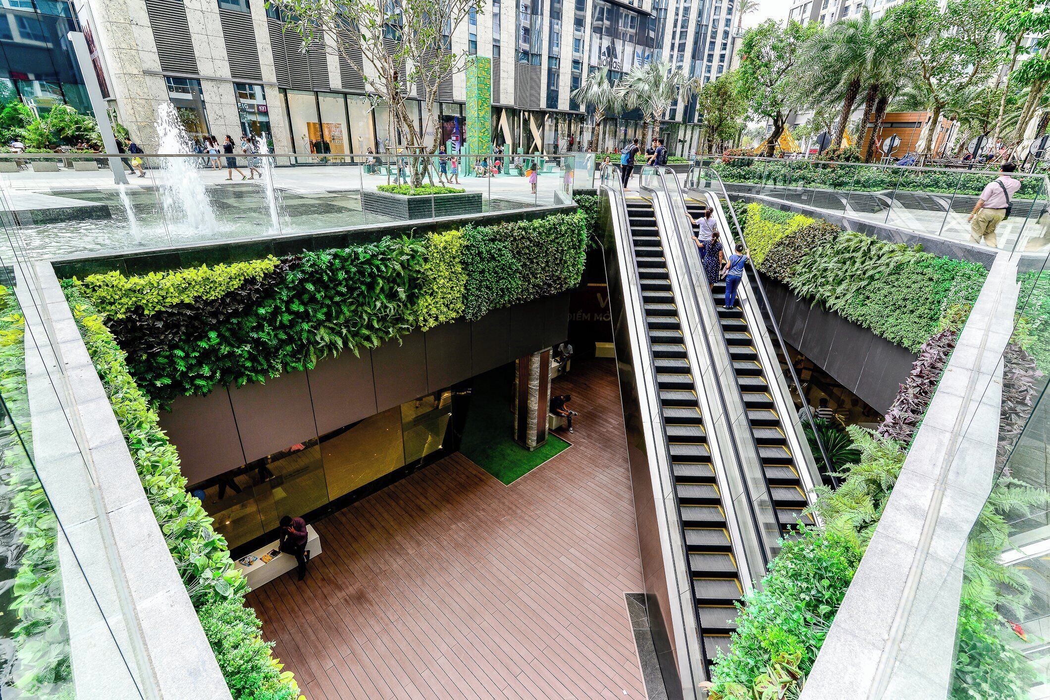 Un atrium interior con una fuente central, escaleras mecánicas y una pared verde con plantas.