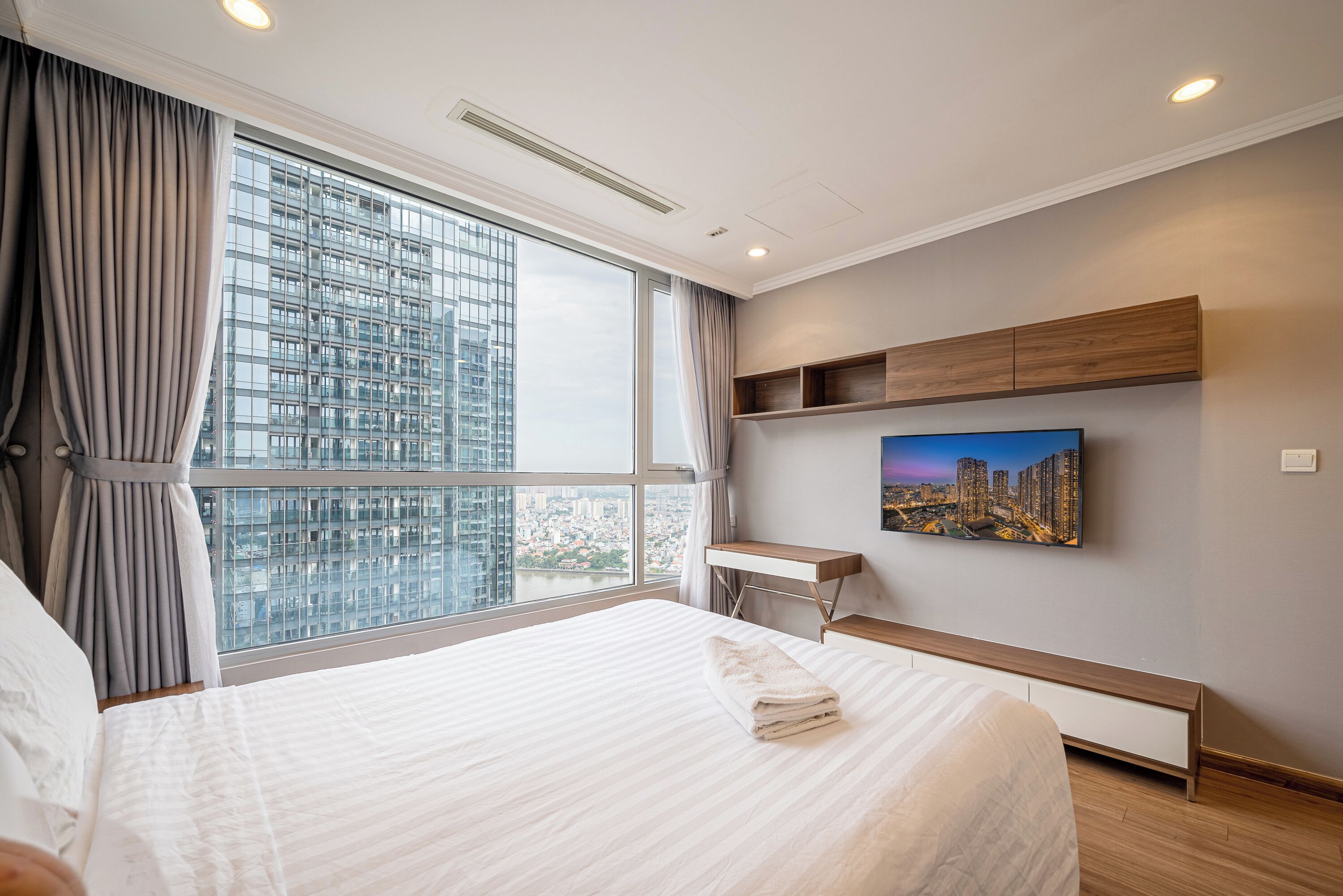 Quarto de hotel com uma cama grande, uma escrivaninha, uma cadeira, uma televisão e vista para a cidade.