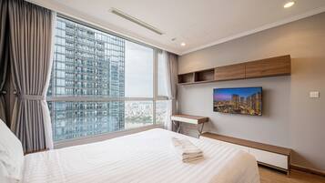 Quarto de hotel com uma cama grande, uma escrivaninha, uma cadeira, uma televisão e vista para a cidade.