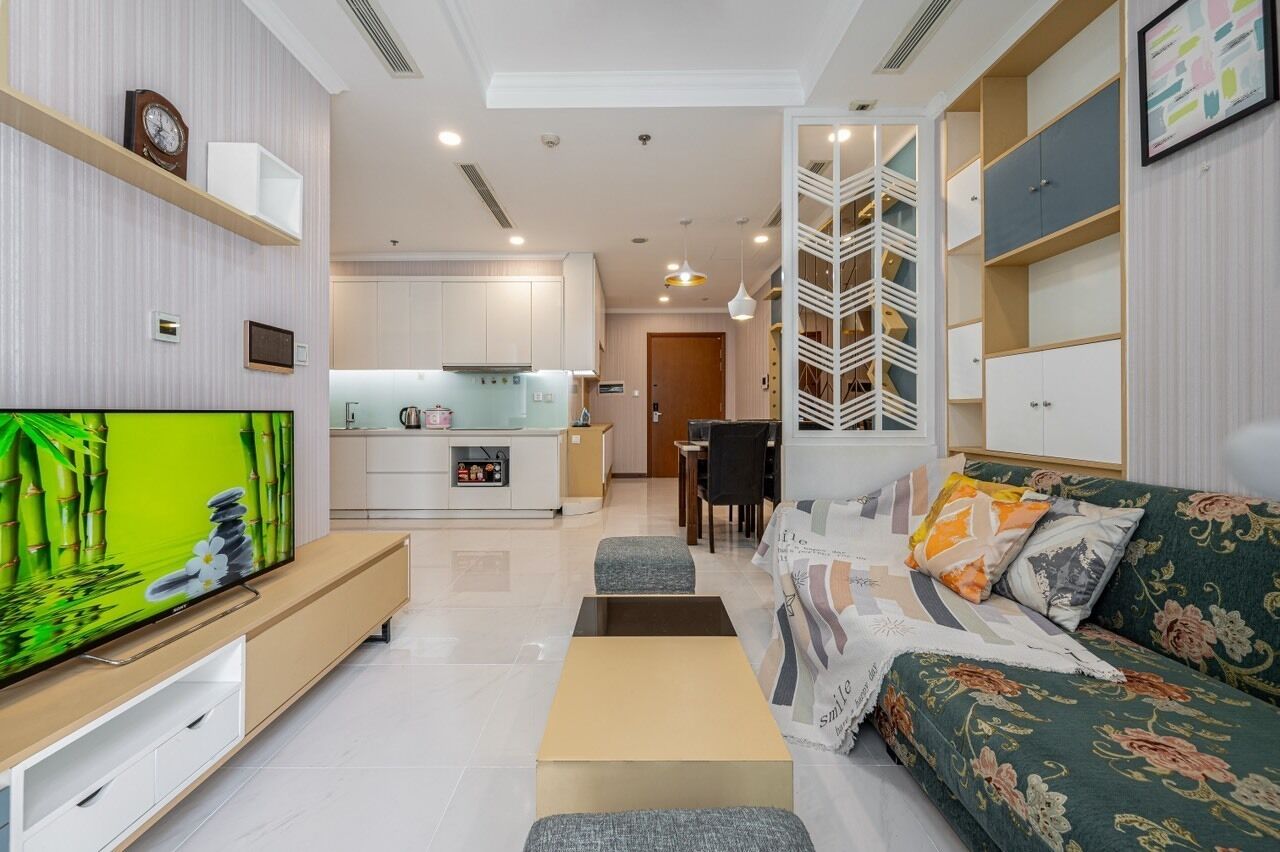 A modern living room with a flat-screen TV, a sofa, a coffee table, and a dining area with a table and chairs.
