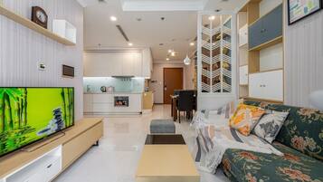 A modern living room with a flat-screen TV, a sofa, a coffee table, and a dining area with a table and chairs.
