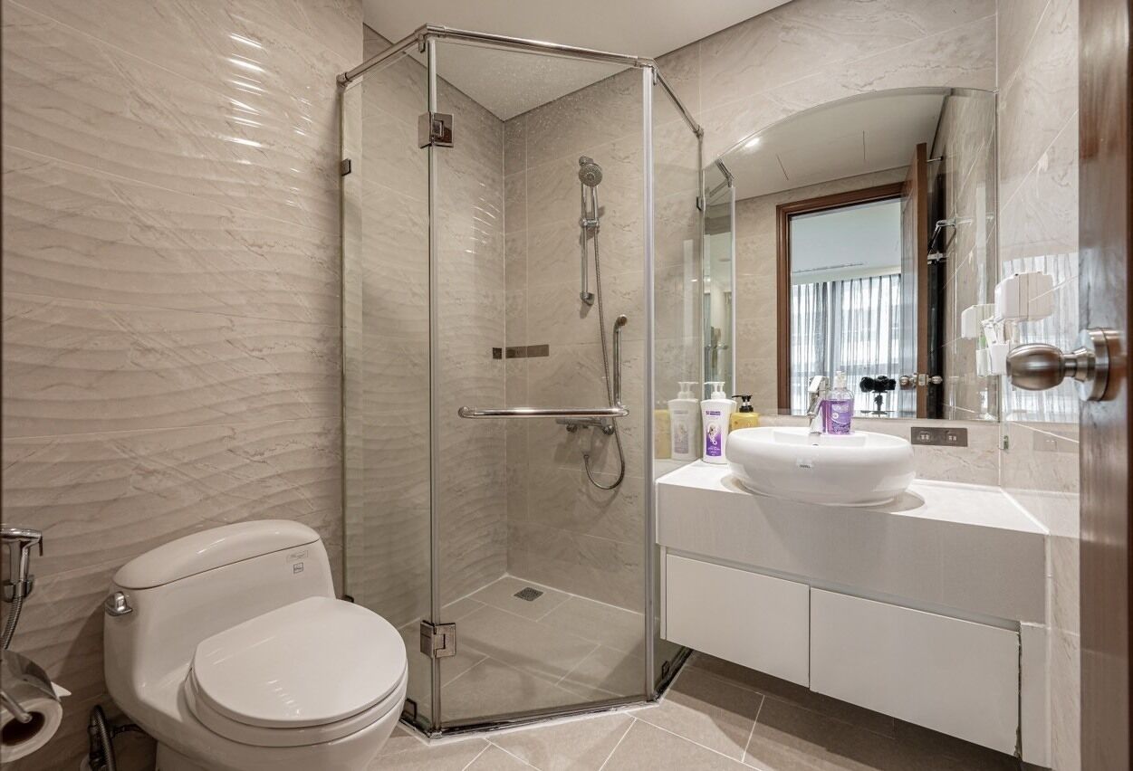 A modern bathroom with a glass-enclosed shower, a white toilet, and a vanity with a sink and mirror.