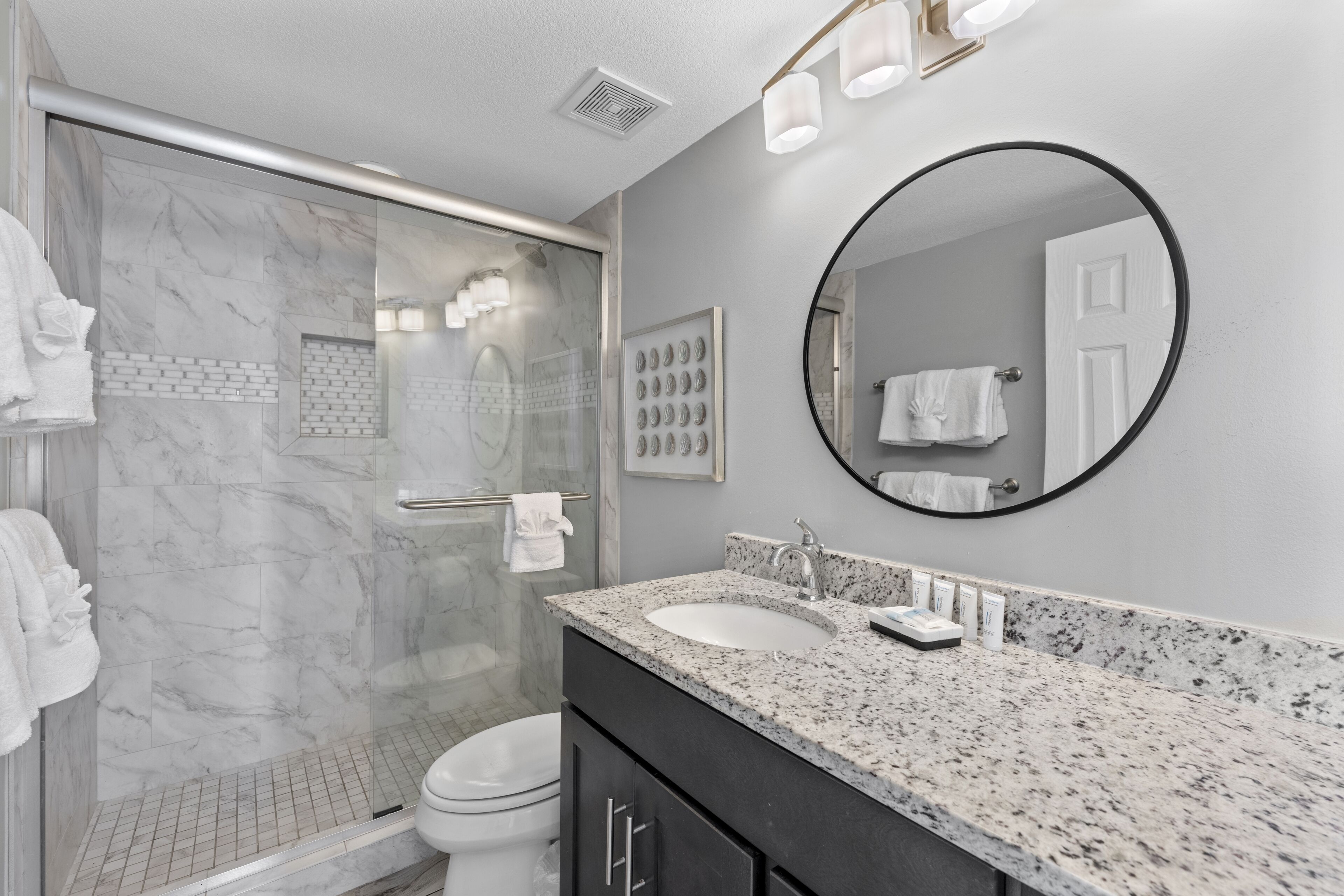 A modern bathroom with a marble shower, a sink with a granite countertop, and a large mirror.