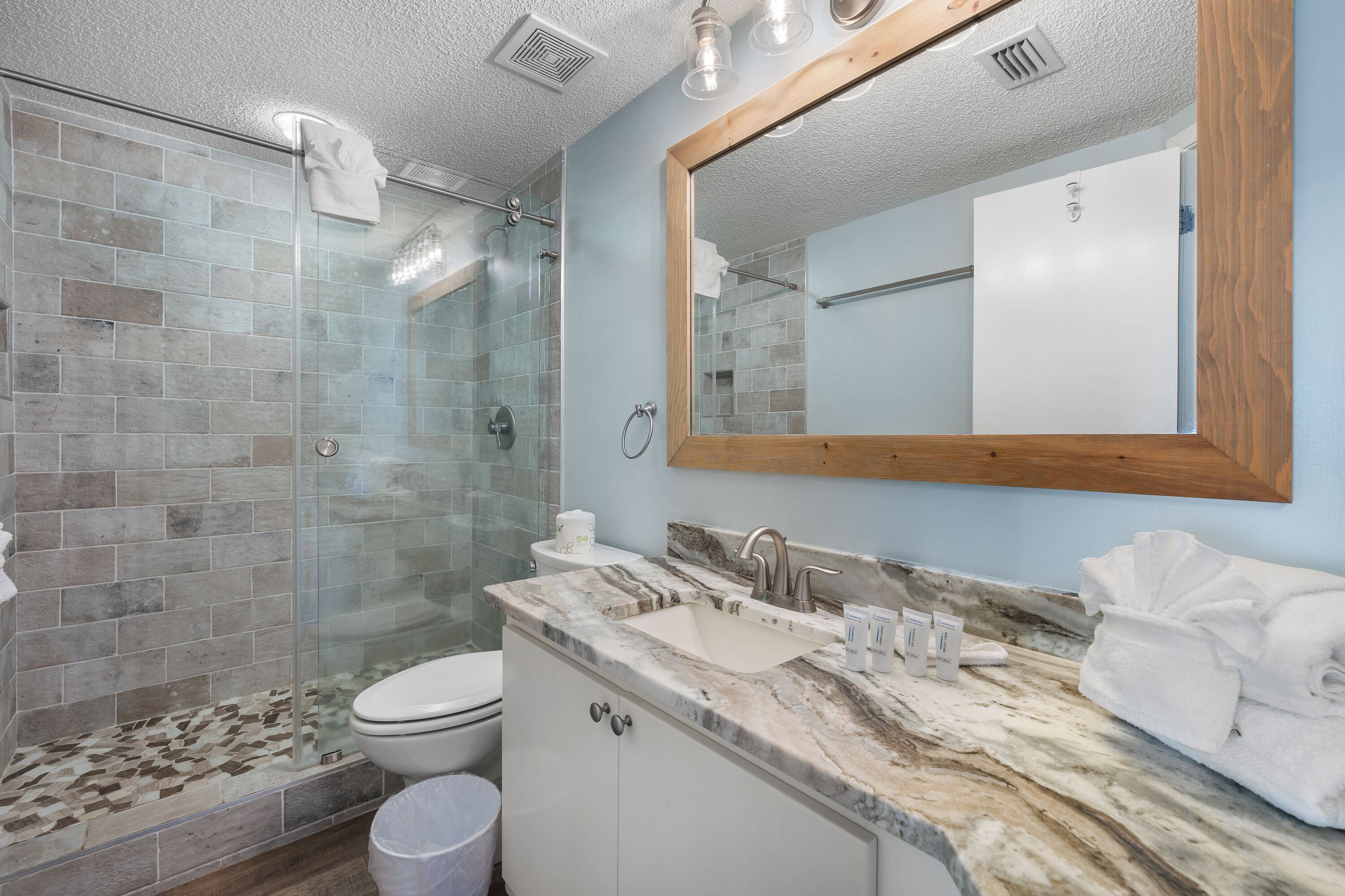 A bathroom with a glass shower enclosure, a sink with a marble countertop, and a large mirror with a wooden frame.