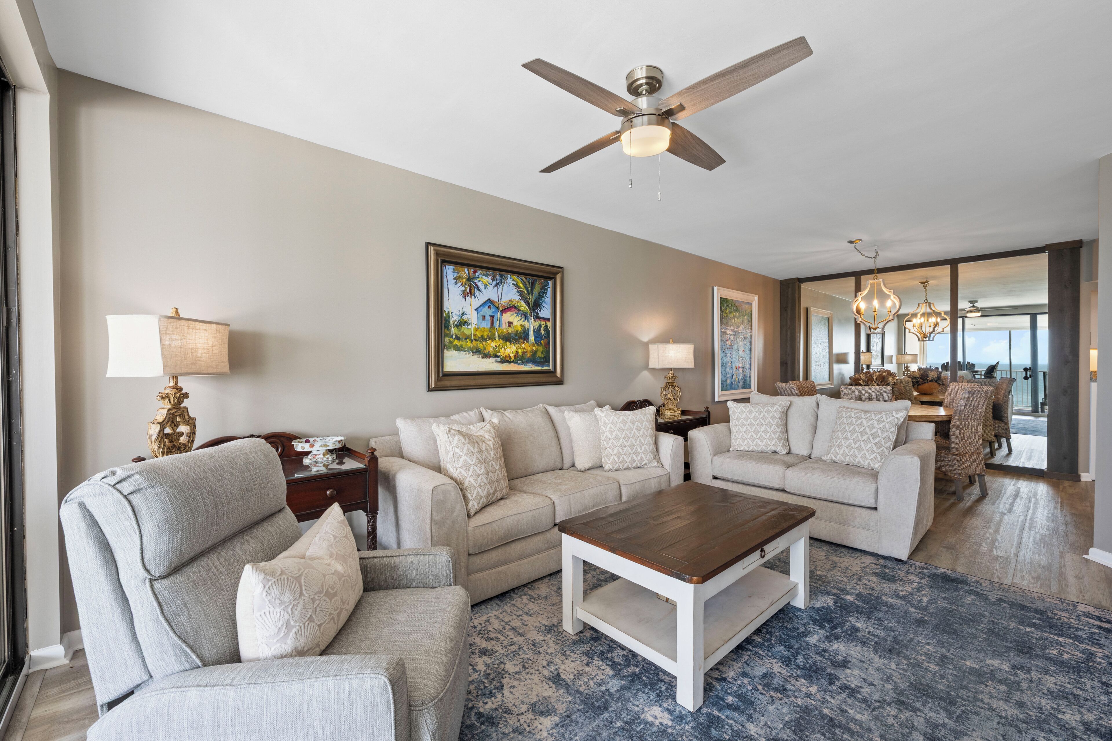 A living room with a sectional sofa, a coffee table, a ceiling fan, and a painting on the wall.