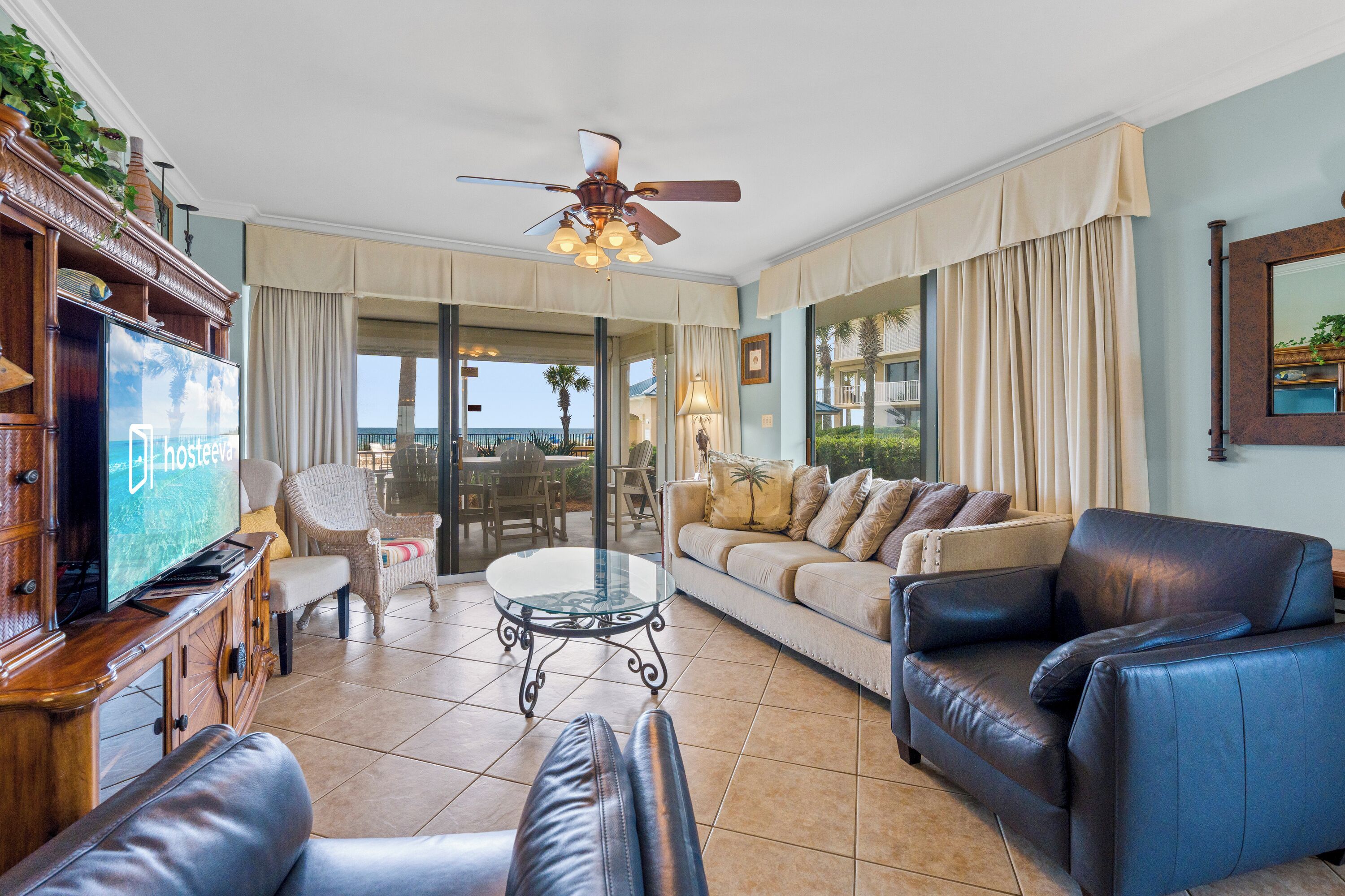 A spacious living room with a television, leather sofas, a glass coffee table, and a ceiling fan.