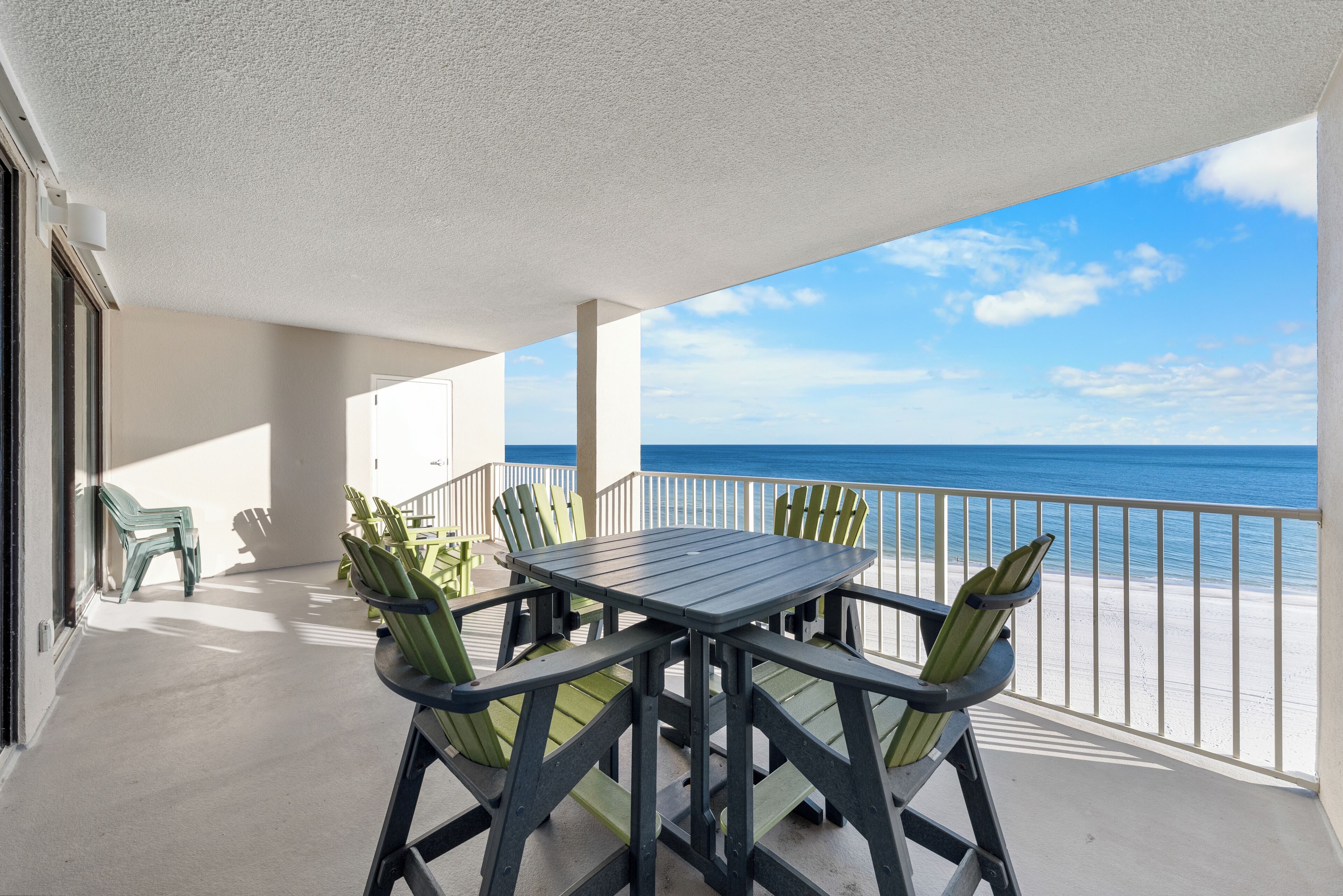 A balcony with a table and chairs, overlooking a beach.