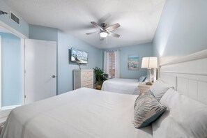 Relax in a serene space with a large bed, ceiling fan, and wall-mounted TV.