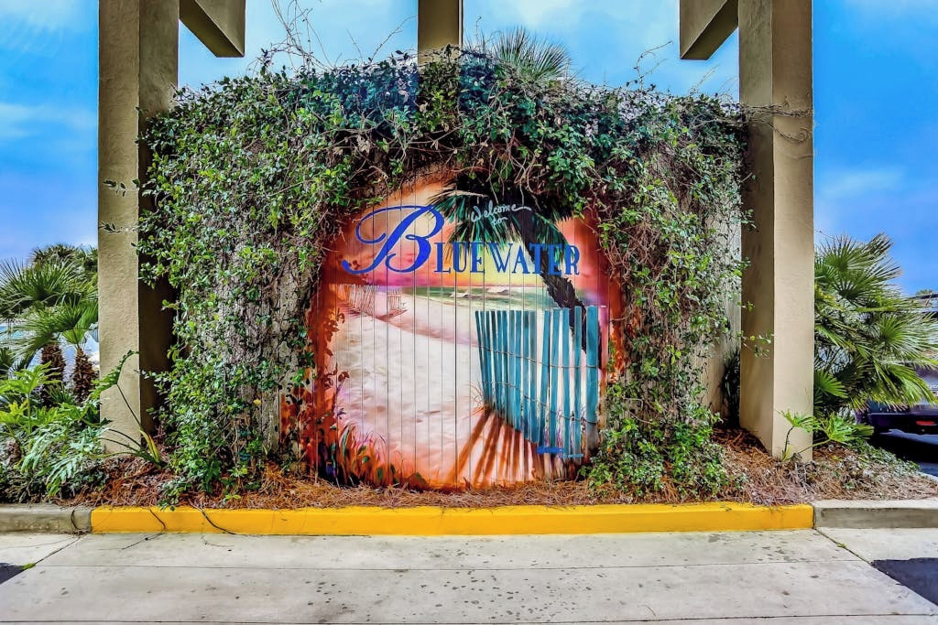 A sign with 'Blue Water' written on it, surrounded by greenery.