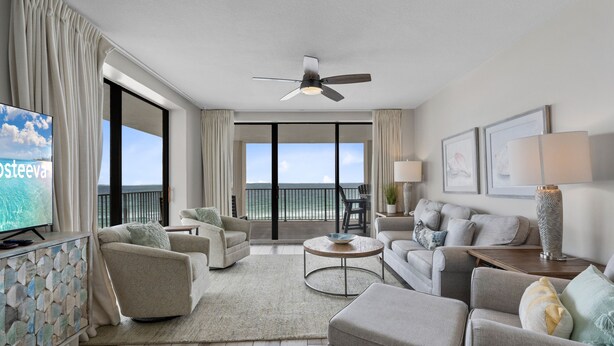Ein geräumiges Wohnzimmer mit Balkon, Deckenventilator und Fernseher.