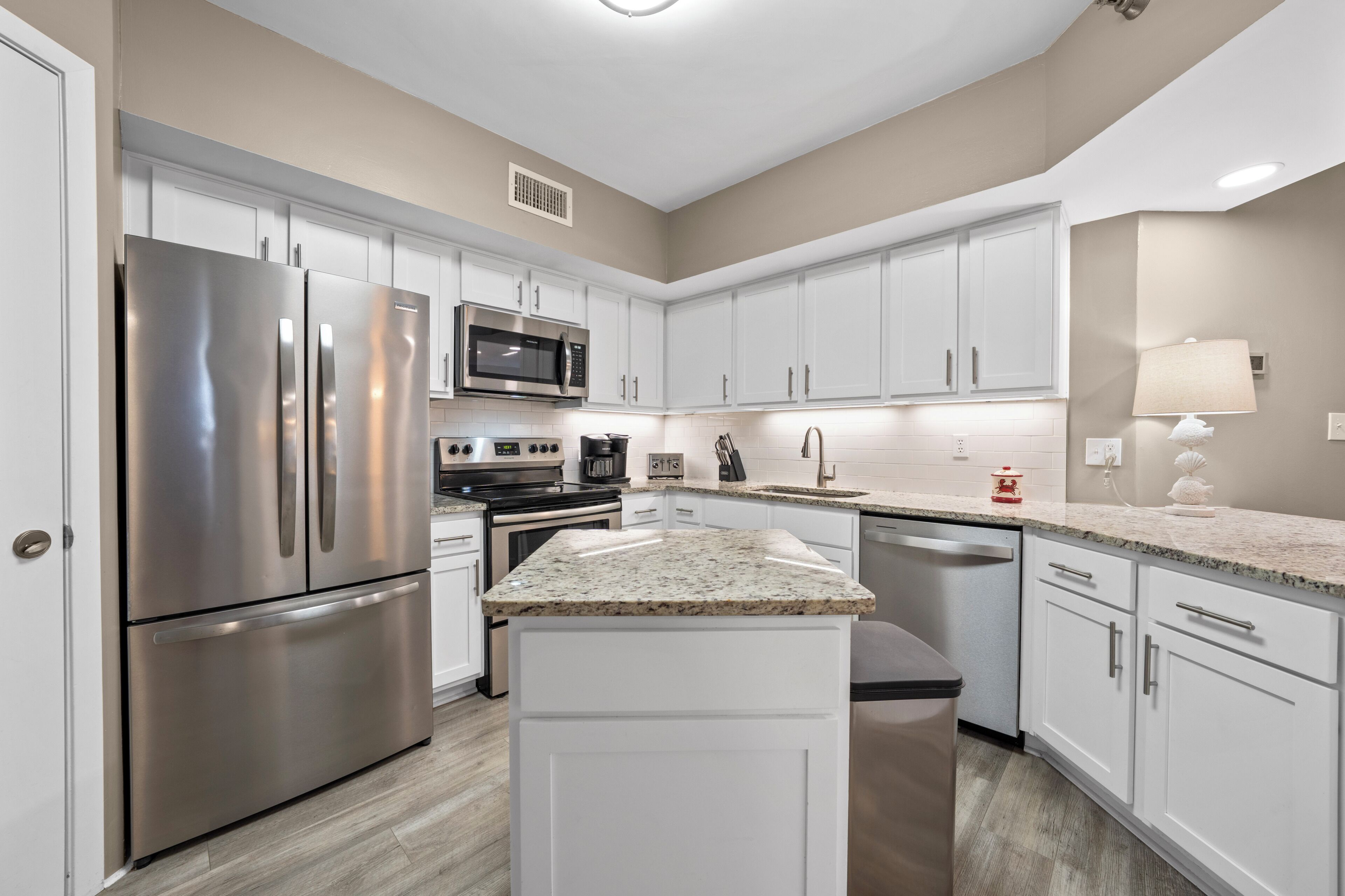 A modern kitchen with stainless steel appliances, white cabinetry, granite countertops, and under-cabinet lighting.