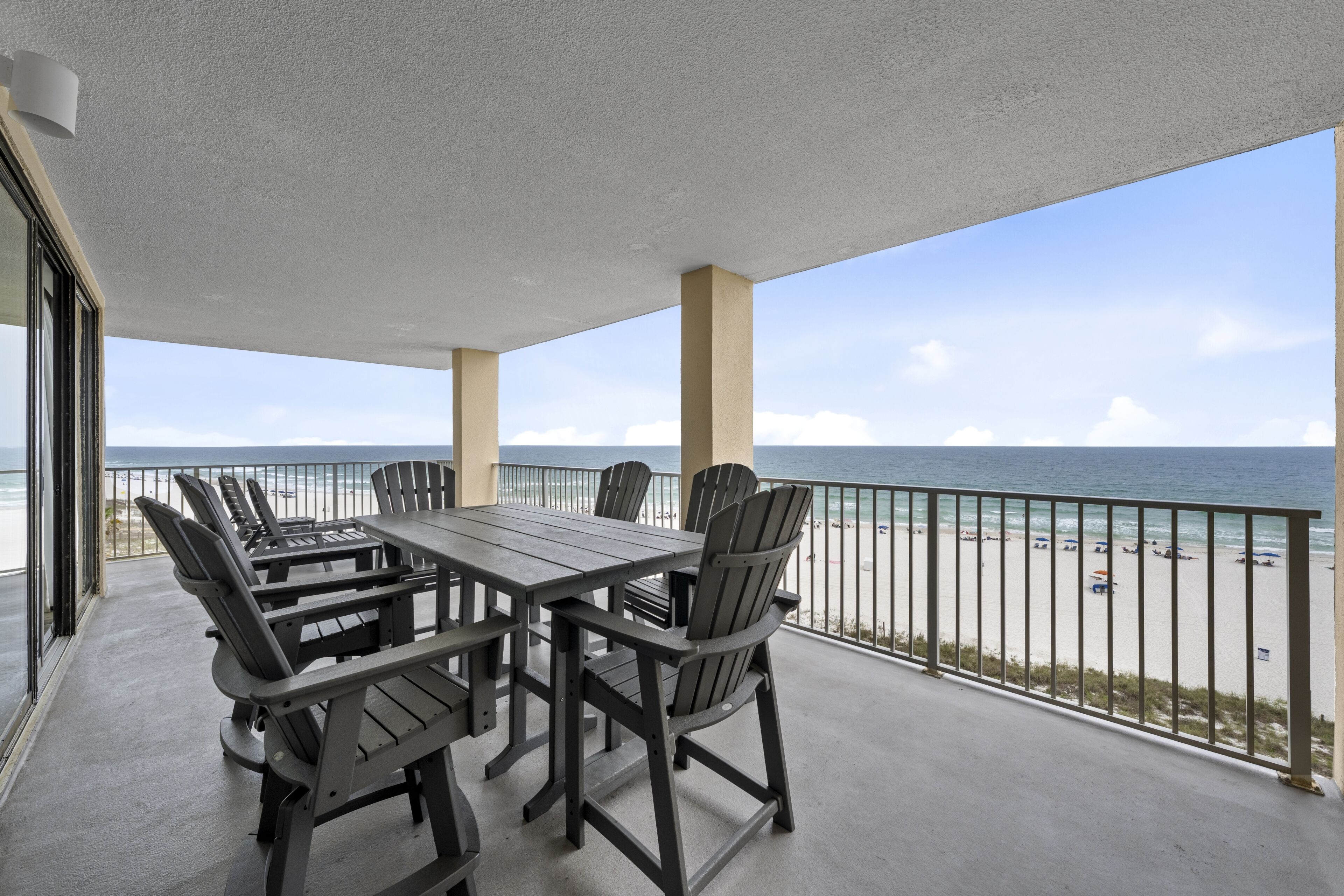 A covered outdoor area with a table and chairs, a view of the beach, and a railing.