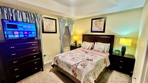 A bedroom with a bed, a dresser, a TV, and two lamps.