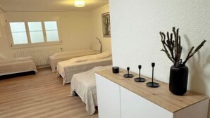 Een kleine, moderne kamer met een houten vloer, een wit kastje met een vaas, en twee bedden.